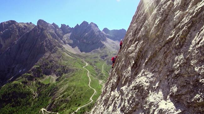© ORF Bergsteiger klettern an steiler Felswand vor grünem Hochtal und Gipfeln der Lienzer Dolomiten.