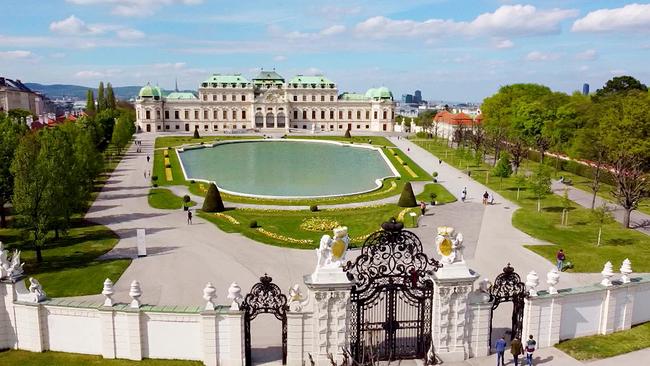 Das Schloss Belvedere mit symmetrischem Garten, großem Wasserbecken und schmiedeeisernem Tor im Vordergrund.