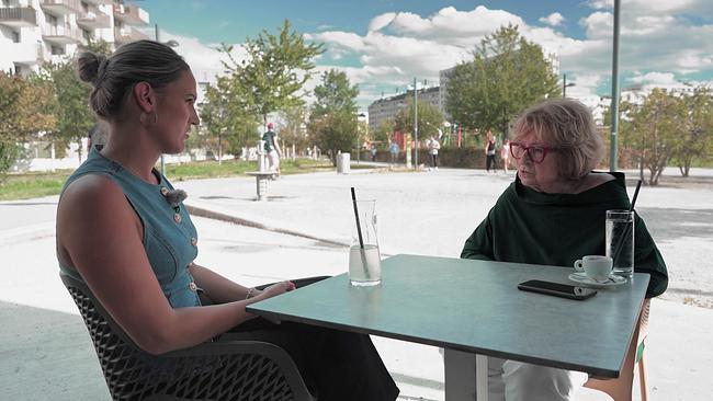 Reporterin Marianne Pušić und eine ältere Dame mit Brille und kinnlangen blonden Haaren sitzen an einem Kaffeehaustisch im Freien - im Hintergrund ein Platz mit Bäumen und Gebäuden