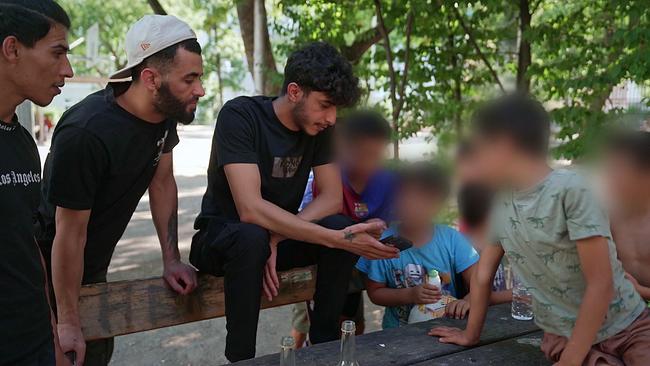 © ORF Gruppe Syrischer Jugendlicher und Kinder sitzen auf einer Parkbank und schauen sich auf einem Handy etwas an