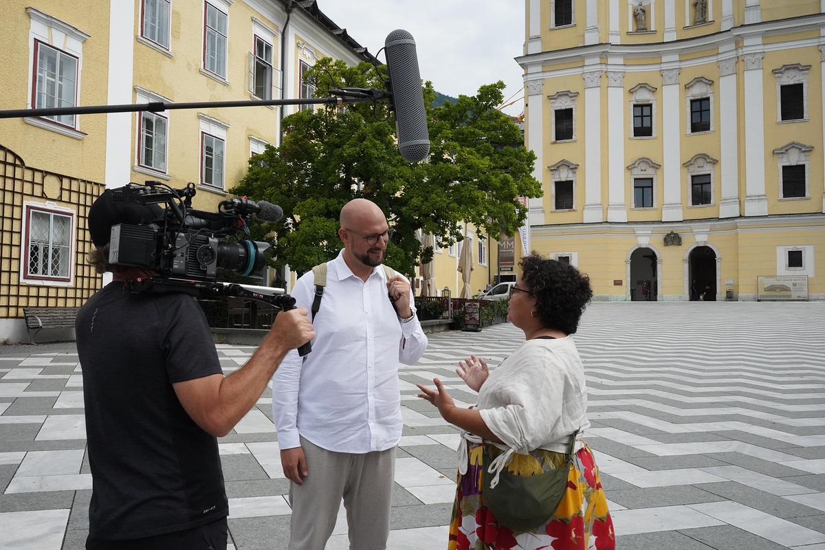 Moderator Sebastian Grandits spricht mit einer holländischen Touristin über The Sound of Music vor der Basilika in Mondsee