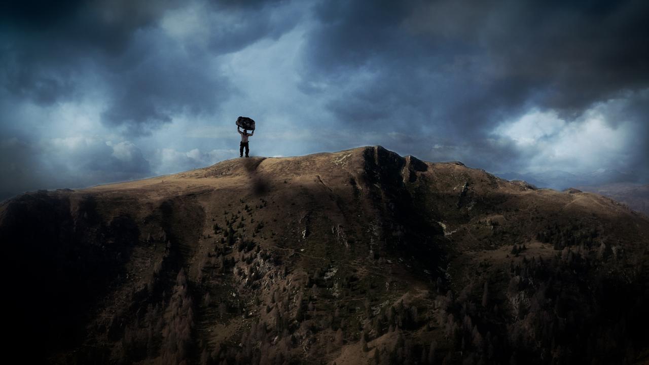 Der Riese steht auf dem Berg Mirnock und hält einen Felsbrocken in die Höhe