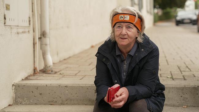 © ORF eine ältere grauhaarige Frau, Brigitta Scharingr, sitzt auf Steinstufen, hinter ihr eine Mauer