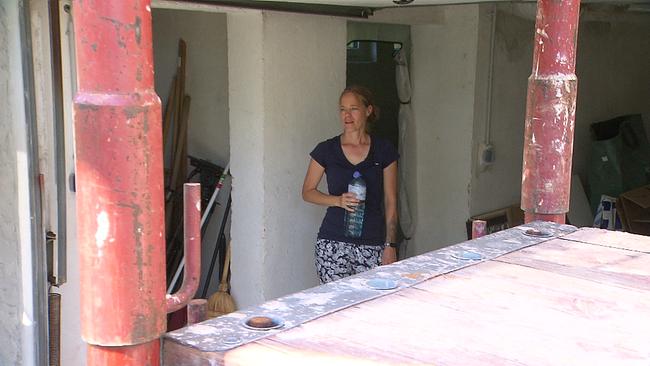 © ORF Baustelle eines Hauses im Vordergrund 2 rote Metallstützen, im Hintergrund eine Mauer mit Türöffnungen, eine junge Frau steht vor der Mauer