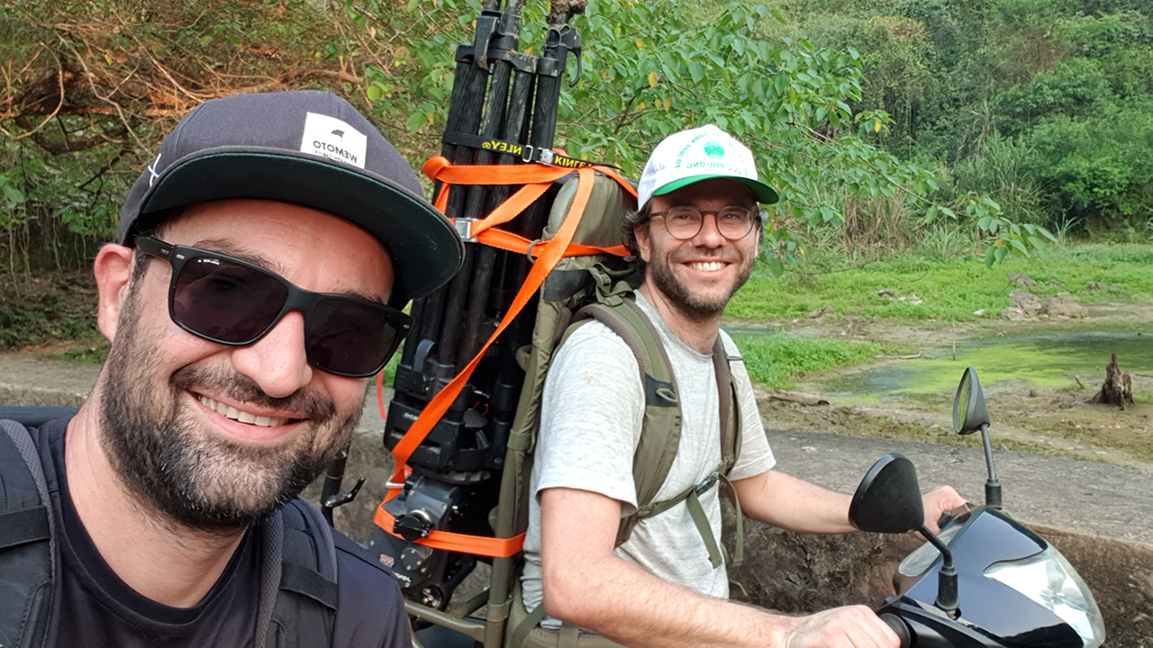 Die beiden Regisseure Johannes Berger und Stephan Krasser jeweils auf einem Moped sitzend. Als Hintergrundkulisse der Dschungel.