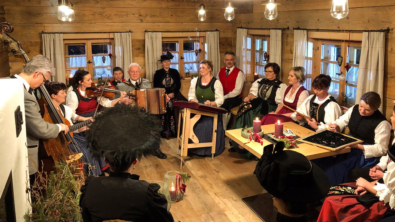 Hausmusik Kraft aus St. Gallenkirch in traditioneller österreichischer Tracht musiziert und sitzt in einer gemütlichen, stimmungsvoll dekorierten Holzstube zusammen.