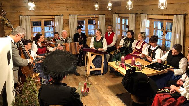 Hausmusik Kraft aus St. Gallenkirch in traditioneller österreichischer Tracht musiziert und sitzt in einer gemütlichen, stimmungsvoll dekorierten Holzstube zusammen.