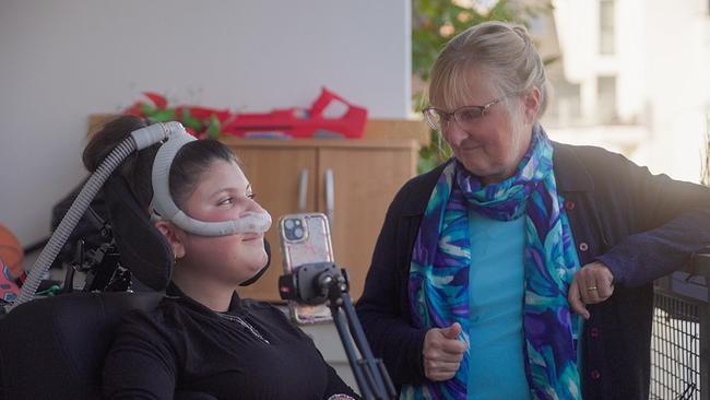 © ORF/Metafilm GmbH Anette Henry steht mit Patientin Khamleen, die mit Beatmungsmaske im Rollstuhl sitzt, auf einer Terrasse.