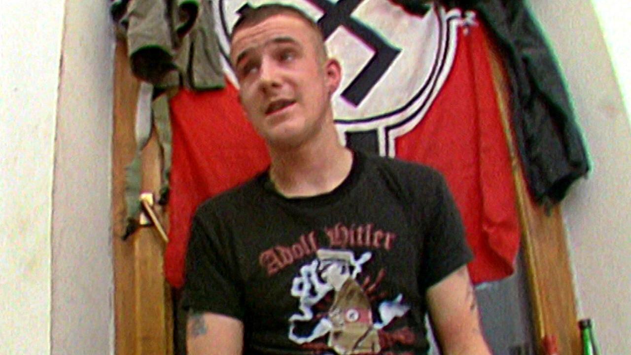 © ORF Skinhead-Neonazi in einem T-Shirt mit Hitler-Motiv vor einer Hakenkreuzfahne, 1992