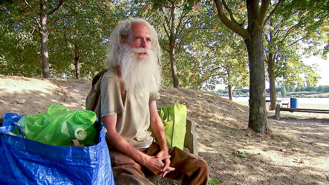 Der Pensionist Florian sitzt auf einer Bank im Schatten von Bäumen auf der Wiener Donauinsel, umgeben von großen Taschen mit Pfandflaschen.