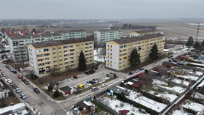 Luftaufnahme der Robert-Stolz-Siedlung mit mehreren mehrstöckigen Wohnhäusern, parkenden Autos und teilweise schneebedeckten Flächen am Rand von Feldern zu sehen.