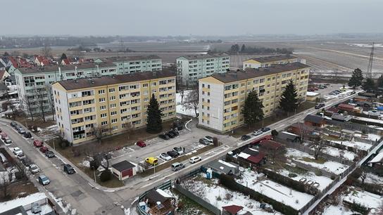 Luftaufnahme der Robert-Stolz-Siedlung mit mehreren mehrstöckigen Wohnhäusern, parkenden Autos und teilweise schneebedeckten Flächen am Rand von Feldern zu sehen.