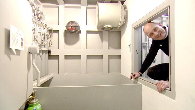 Stanislav Miklic, Verkaufsleiter für Luxusbunker, blickt durch eine Öffnung in einen hellen technischen Raum mit Lüftungs- und Messgeräten an der Wand