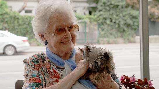 Frau Gerda, 95 Jahre, sitzt mit ihrem Hund Lena in einem Wintergarten. Sie vermacht ihr gesamtes Vermögen dem Tierschutz.