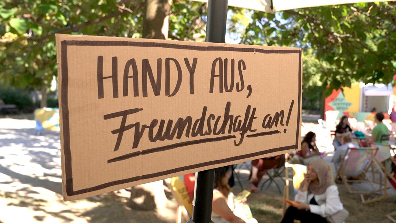 © ORF Ein handbeschriftetes Schild mit der Aufschrift „Handy aus, Freundschaft an!“ wirbt bei einer Veranstaltung im Freien für ein Offline Event.