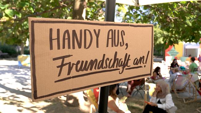 © ORF Ein handbeschriftetes Schild mit der Aufschrift „Handy aus, Freundschaft an!“ wirbt bei einer Veranstaltung im Freien für ein Offline Event.