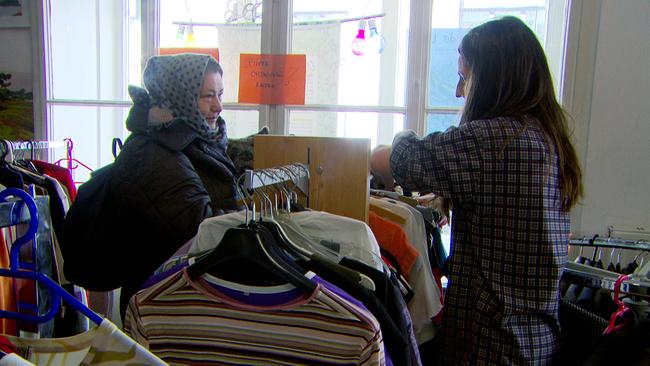 Am Bild sind zwei Frauen, die im Kostnix Laden in Salzburg zwischen einigen gut gefüllten Kleiderständern stehen.
