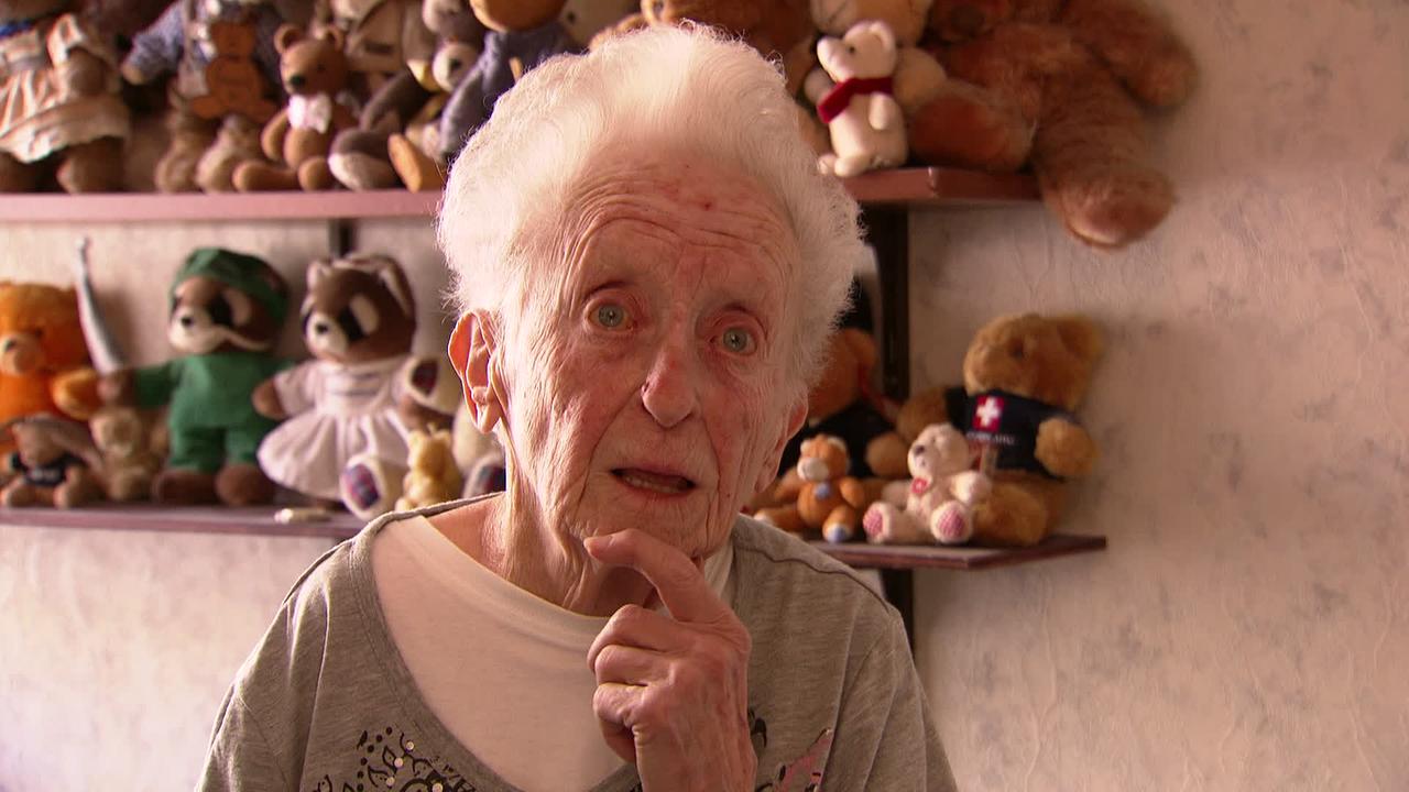 Am Bild ist Frau Rosa, eine alte weißhaarige Frau. Im Hintergrund ist ihre Teddy-Sammlung.