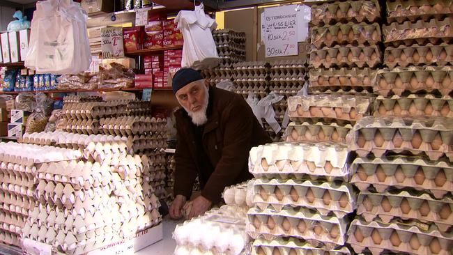 Am Bild ist ein Mann mit weißem Bart inmitten von vielen Eierkartons am Markt.