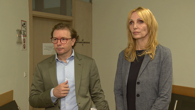 Ein Mann und eine Frau stehen im Wartebereich eines Gerichtssaals.