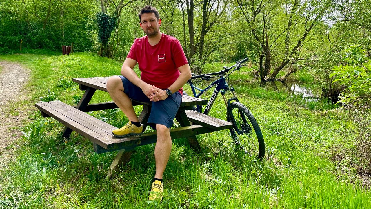 Koch Werner Punz sitzt auf einer Holzbank in einer grünen Aulandschaft an der Traisen.