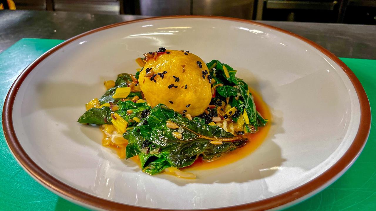 Vegetarischer Topinambur-Grammelknödel auf warmem Mangoldsalat mit Schwarzkümmelsauce auf weißem Teller angerichtet.