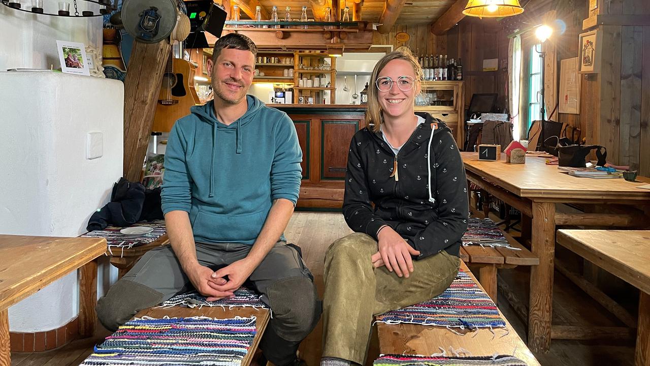 © ORF/Satel Film/David Haslinger Stefan und Christina Rindler sitzen nebeneinander auf einer Bank in der rustikalen Gaststube ihrer Almhütte.