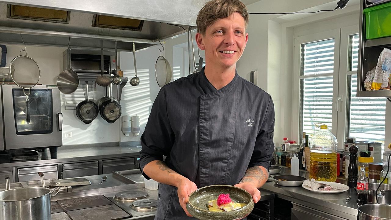 © ORF/Satel Film/David Haslinger Jakob Lilg steht in der Restaurantküche Löwenzahn und hält einen Teller mit eingelegter Rotfeder