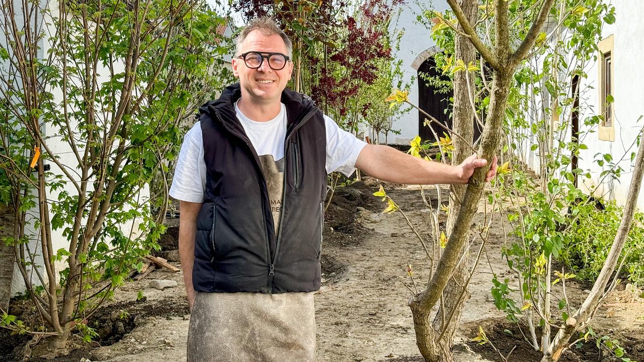 Koch Max Stiegl bei einem Baum im Garten seines Restaurants. 
