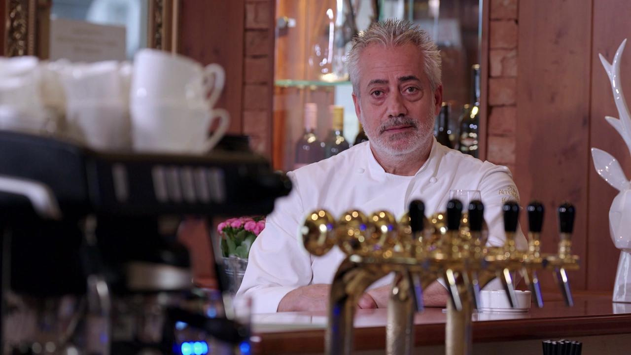 Metin Yurtseven in weißer Kochjacke sitzt hinter einer Theke  des Restaurants „Zum alten Beisl“.