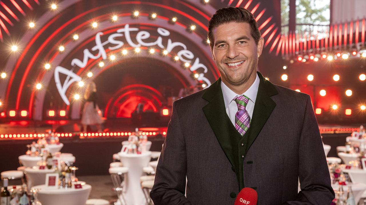 © ORF/Regine Schöttl Norbert Oberhauser lächelt in die Kamera vor der Bühne von "Aufsteirern - Die Show der Volkskultur"