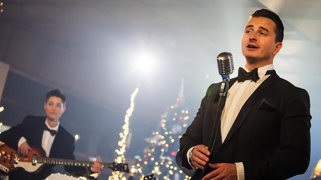 © ORF/Landesstudio Steiermark/Regine Schöttl Andreas Gabalier im Smoking performt vor einem Mikrofon, während im Hintergrund eine Band und weihnachtliche Dekoration zu sehen sind.