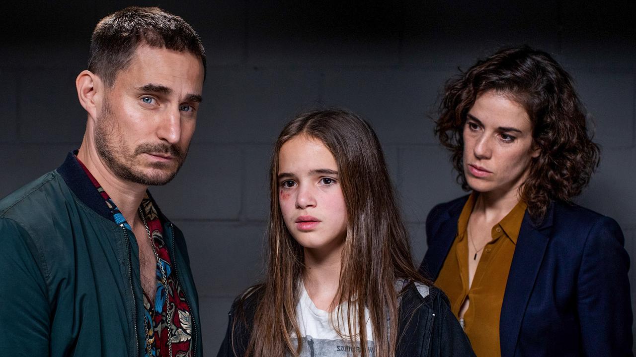 Ein Mann, ein Mädchen und eine Frau stehen dunkel gekleidet nebeneinander und blicken erschüttert und nachdenklich drein