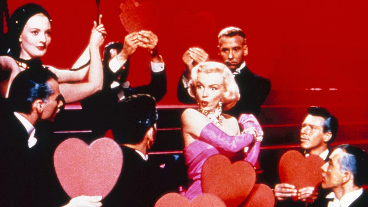 Marilyn Monroe als Lorelei Lee bei einem Auftritt in rosafarbenem Abendkleid mit reichlichem Diamantenschmuck, umgeben von Tänzern in Fräcken, die ihr rote Herzen entgegenhalten