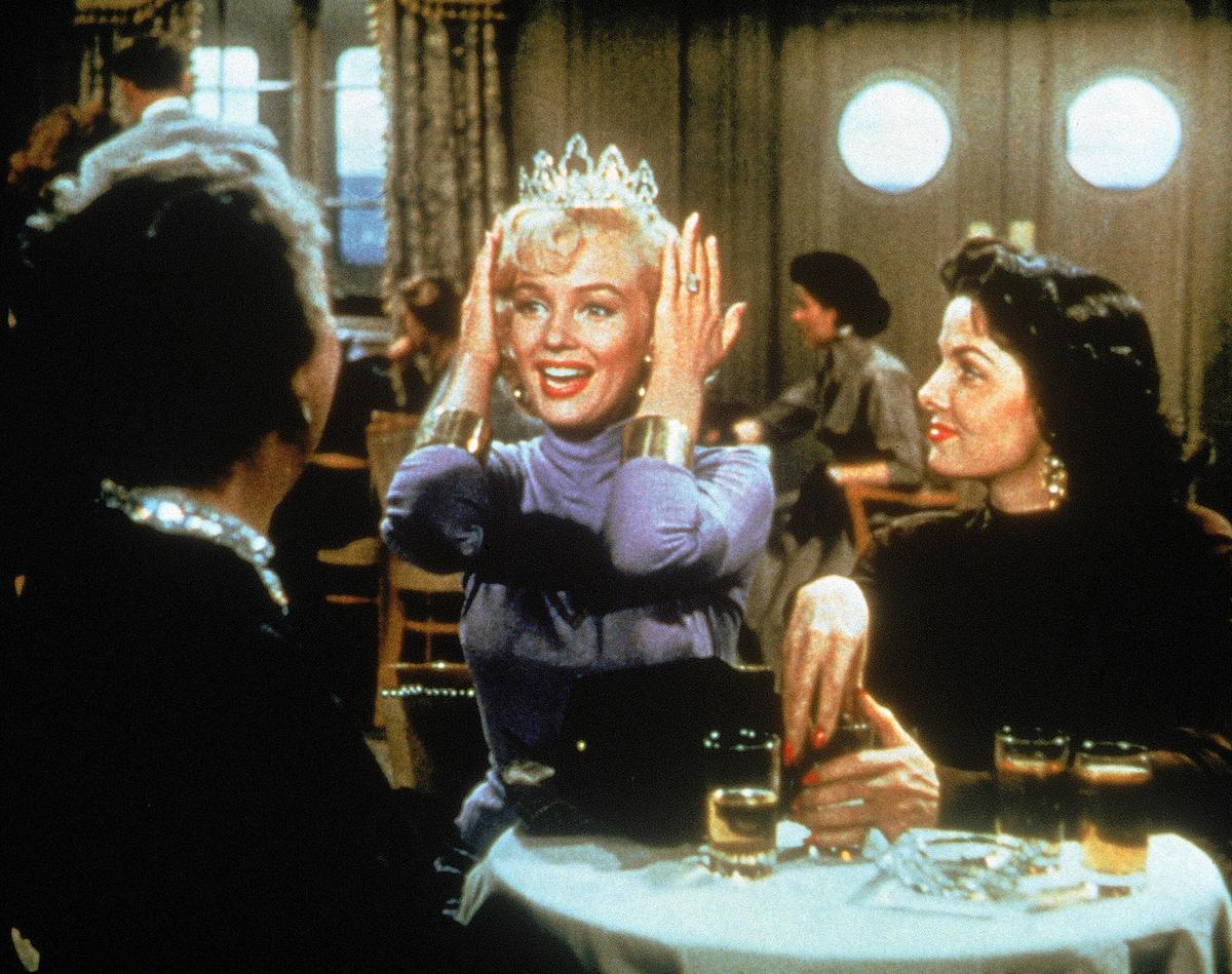 Marilyn Monroe hält sich als Lorelei überglücklich ein Diamant-Diadem auf den Kopf, Jane Russell sitzt als Dorothy Shaw neben ihr und sieht ihr von der Seite zu