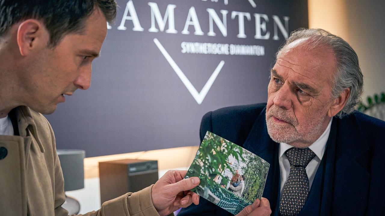 © Foto: ORF/Degeto/Martin Mlaka Im Bild: Borchert (Christian Kohlund, re.) zeigt seinem Mandanten Xavier Schliemann (David Rott, li.) ein Foto.