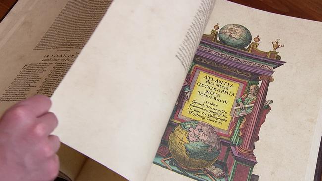 Am Bild blättert jemand in einem großen Buch. Auf der zu sehenden Seite ist eine bunte Zeichnung mit Globus und als Überschrift steht: Atlantis pars altcra Geographia nova Totius mundi.