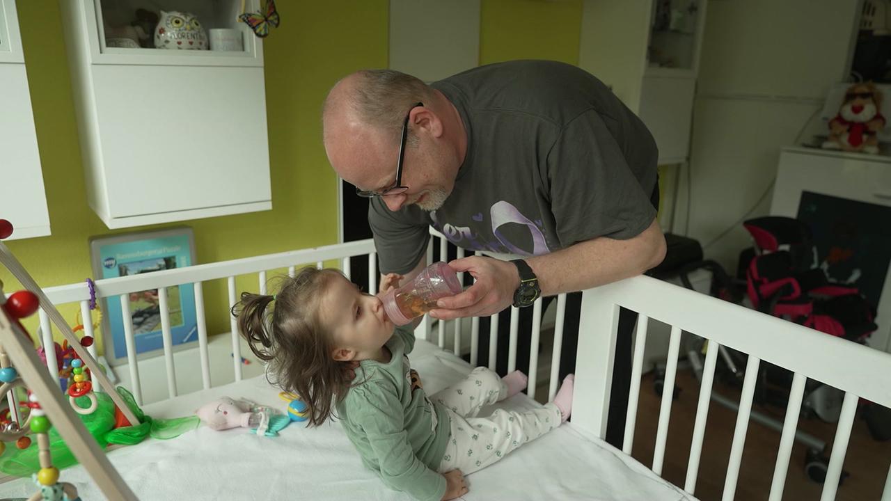 Man sieht das Kleinkind mit dem Vater beim Trinken aus dem Fläschchen.