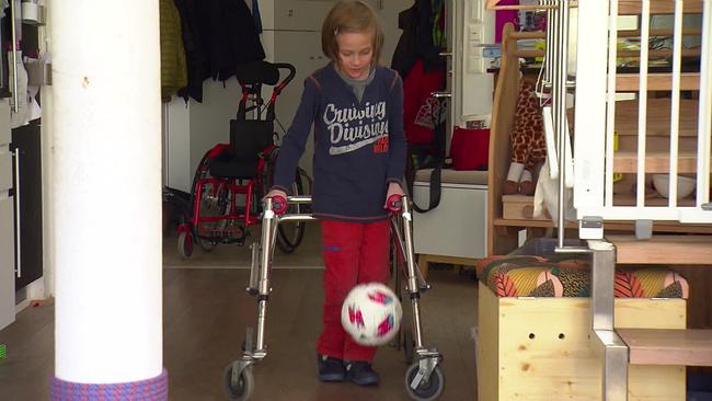 Ein Bub versucht in der Wohnung mit seinem Rollator Fussball zu spielen.