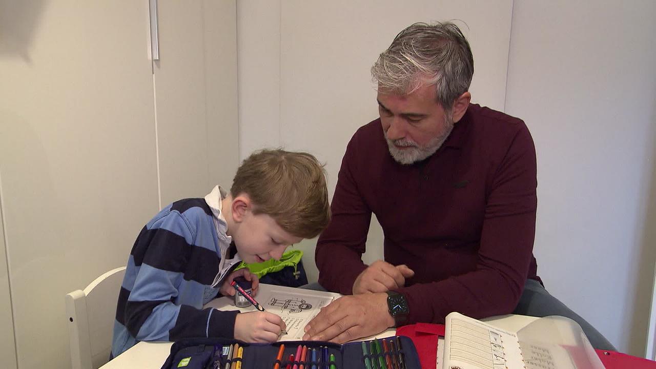 Am Bild macht ein Bub zusammen mit seinem Vater Hausaufgaben.