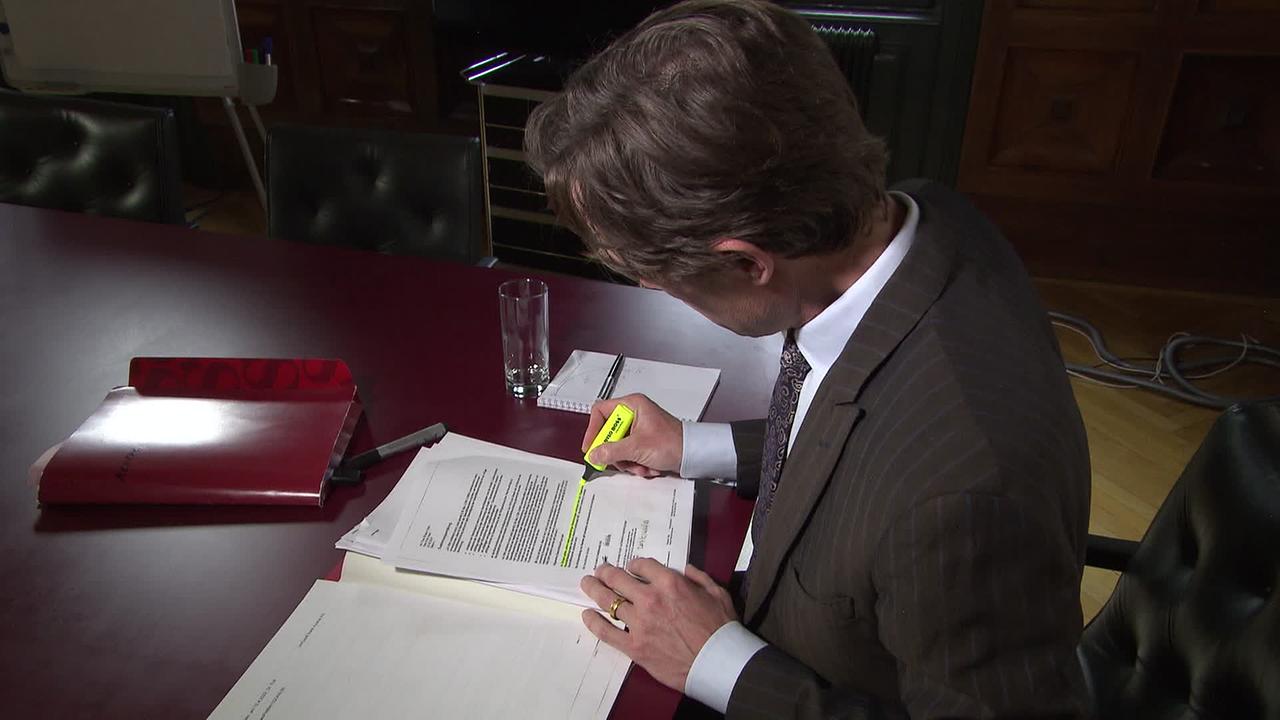 Am Bild ist ein Anwalt, der mit einem gelben Marker Textpassagen in einem Schriftstück markiert.