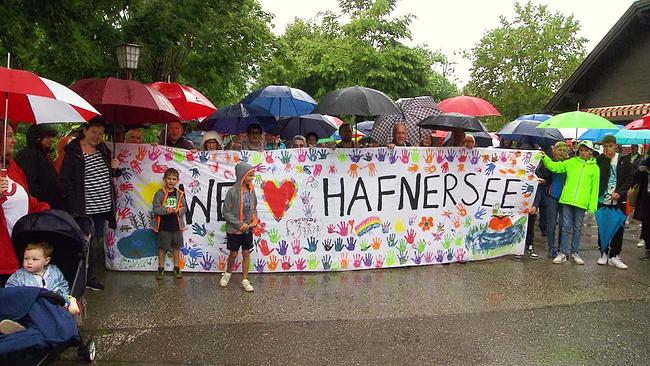 Am Bild ist ein Transparent zu sehen, mit der Aufschrift: We love Hafnersee. Rundherum viele Dauercamper, die gegen die Räumung des Campingplatzes demonstrieren. 
