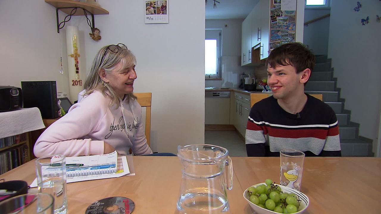 Am Bild sind Gerhard, ein 23jähriger junger Mann, mit seiner Mutter am Esstisch zu sehen. Beide lachen.