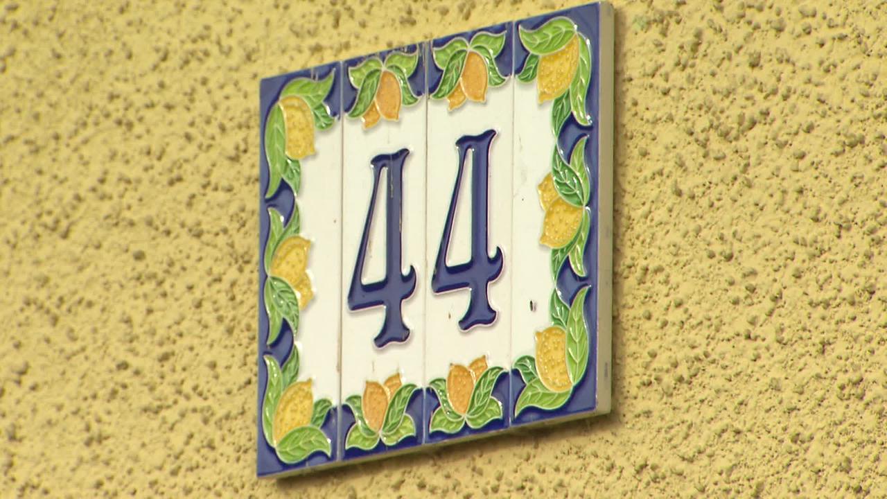 Am Bild ist eine Hausnummer 44 auf bunt verzierter Fliese zu sehen. Das Haus auf dem die Nummer hängt, ist gelb.