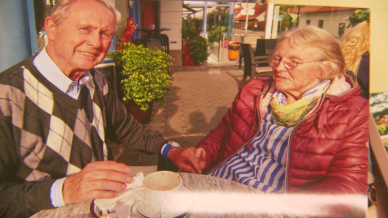 Am Bild sind Herr und Frau H. beim Kaffeetrinken auf einer Terrasse. Sie halten sich dabei an der Hand und lächeln.