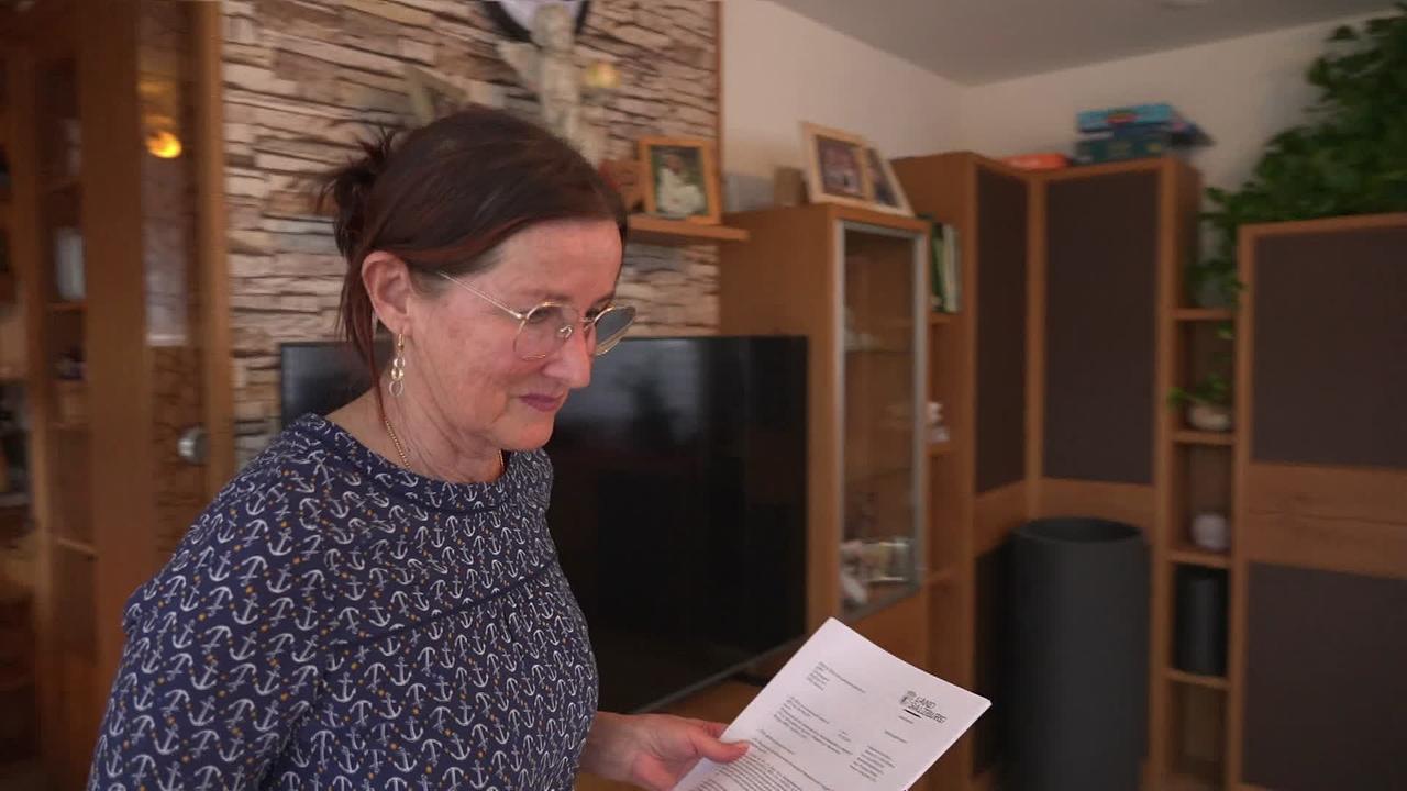 Am Bild ist Frau M., eine pensionierte Pflegekraft, in ihrer Wohnung. In der Hand hält sie ein Schreiben vom Land Salzburg.