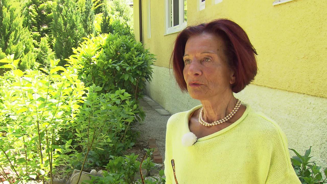 Frau P., eine Pensionistin steht vor ihrem Haus im Garten. 