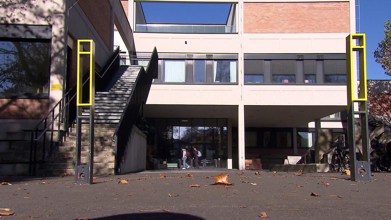 Am Bild ist das Gymnasium in Feldbach von außen zu sehen. Ein paar Kinder gehen gerade ins Gebäude.