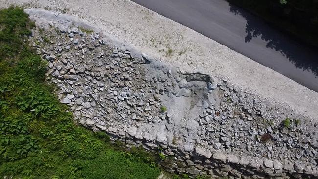 Am Bild ist eine massive Stützmauer aus Steinen neben einer Straße zu sehen.