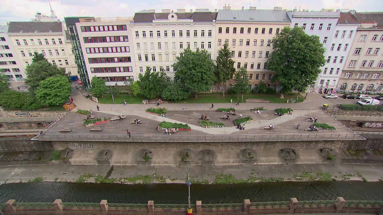 Am Bild ist eine Terrasse zu sehen, die über dem Wienfluss liegt. Im Hintergrund sind mehrstöckige Wohnhäuser zu sehen. Die Anrainer/innen sehen genau auf die Terrasse hinunter.